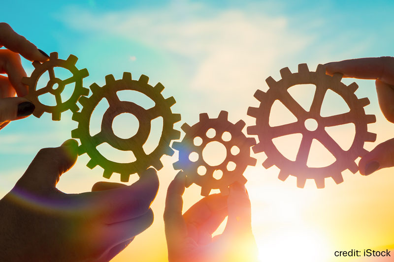 Hands holding cogwheels together, silhouetted against sky
