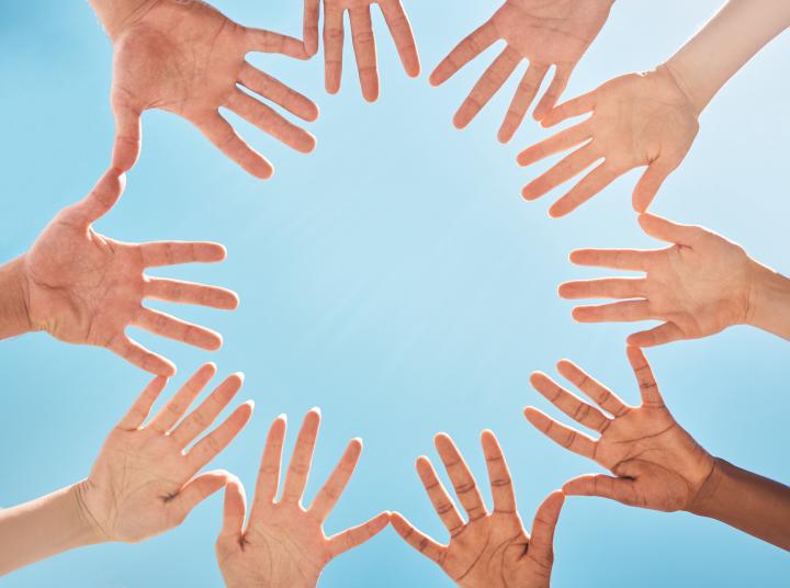 Hands joined to form a circle, seen from below with a blue sky in the background
